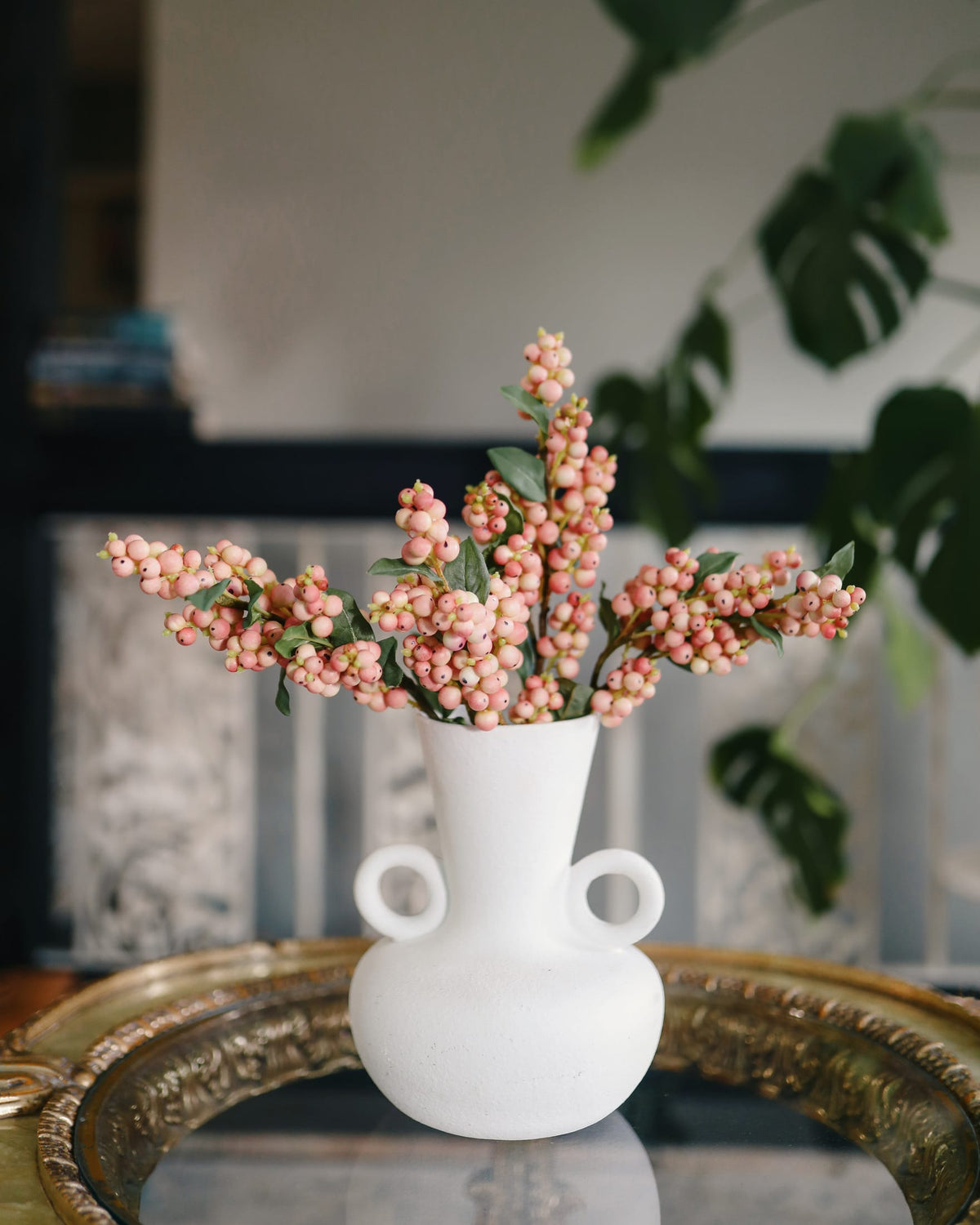 White vase with faux pink berry arrangement on a reflective surface