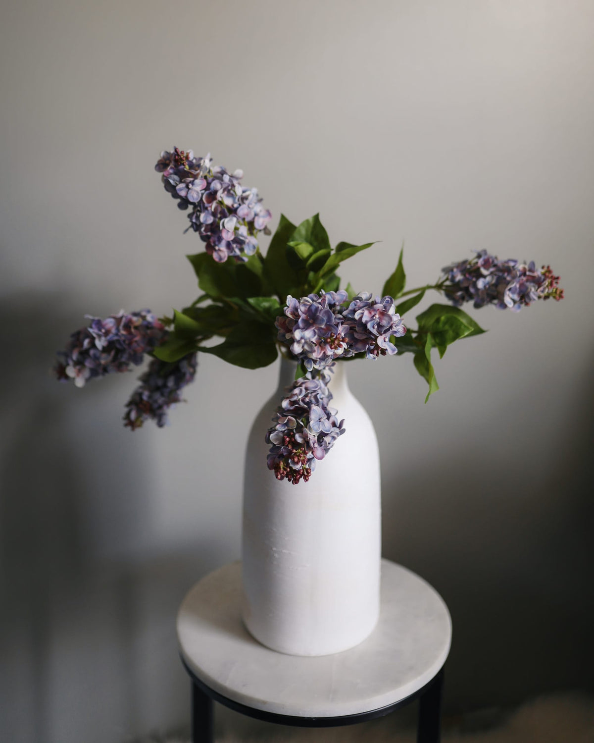 White vase with purple faux lilac on a gray background
