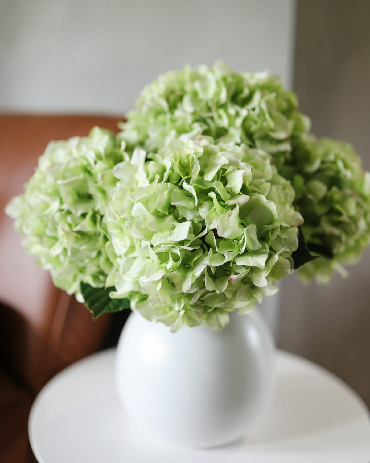 Light green faux hydrangeas in a white vase on a neutral background