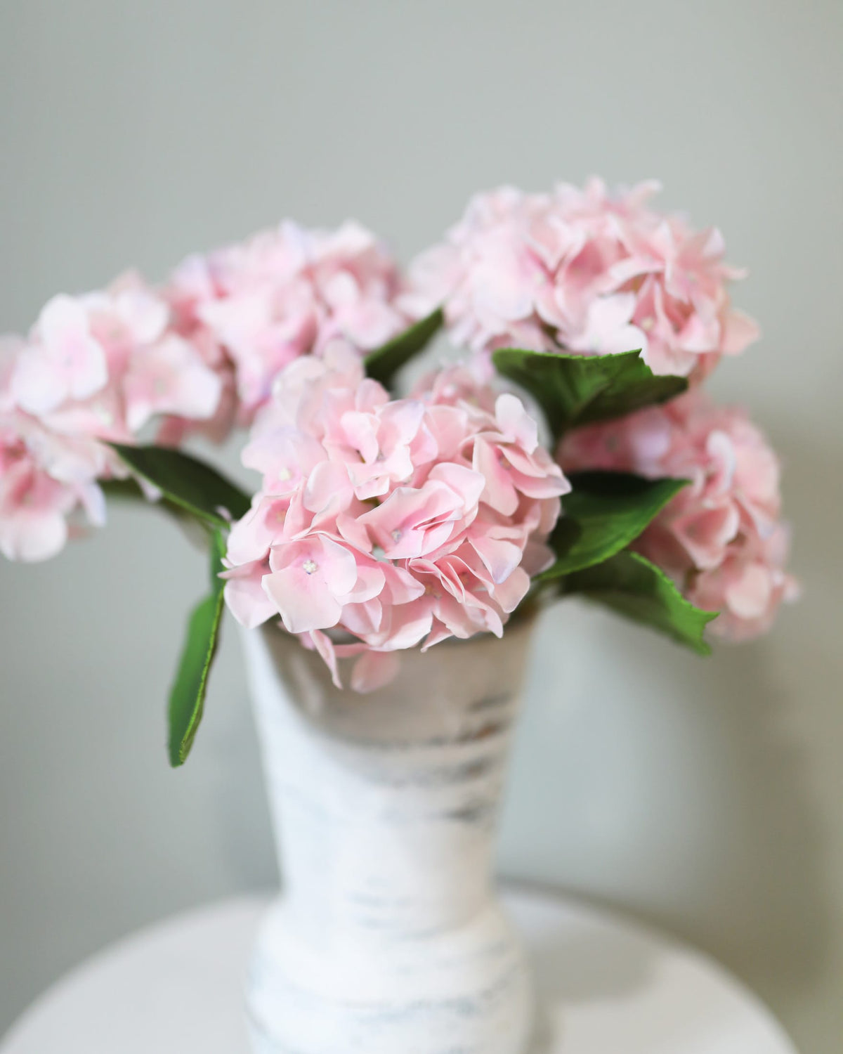 Pink faux hydrangeas in a white vase on a light gray background