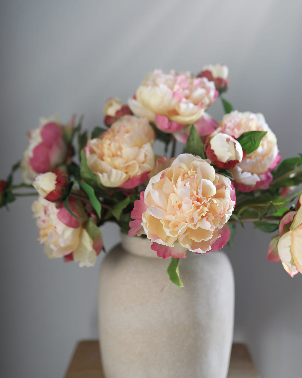 Bouquet of faux pink and white peonies in a beige vase against a gray background