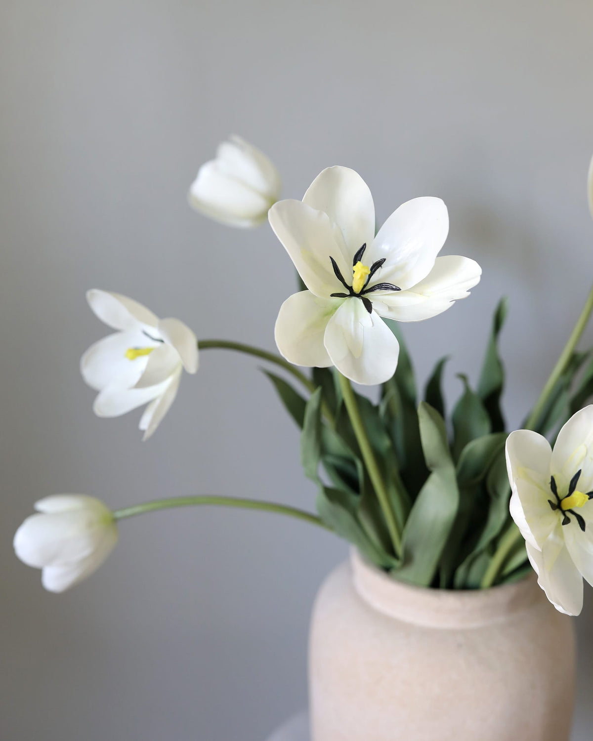 Faux White tulips in a vase against a gray background