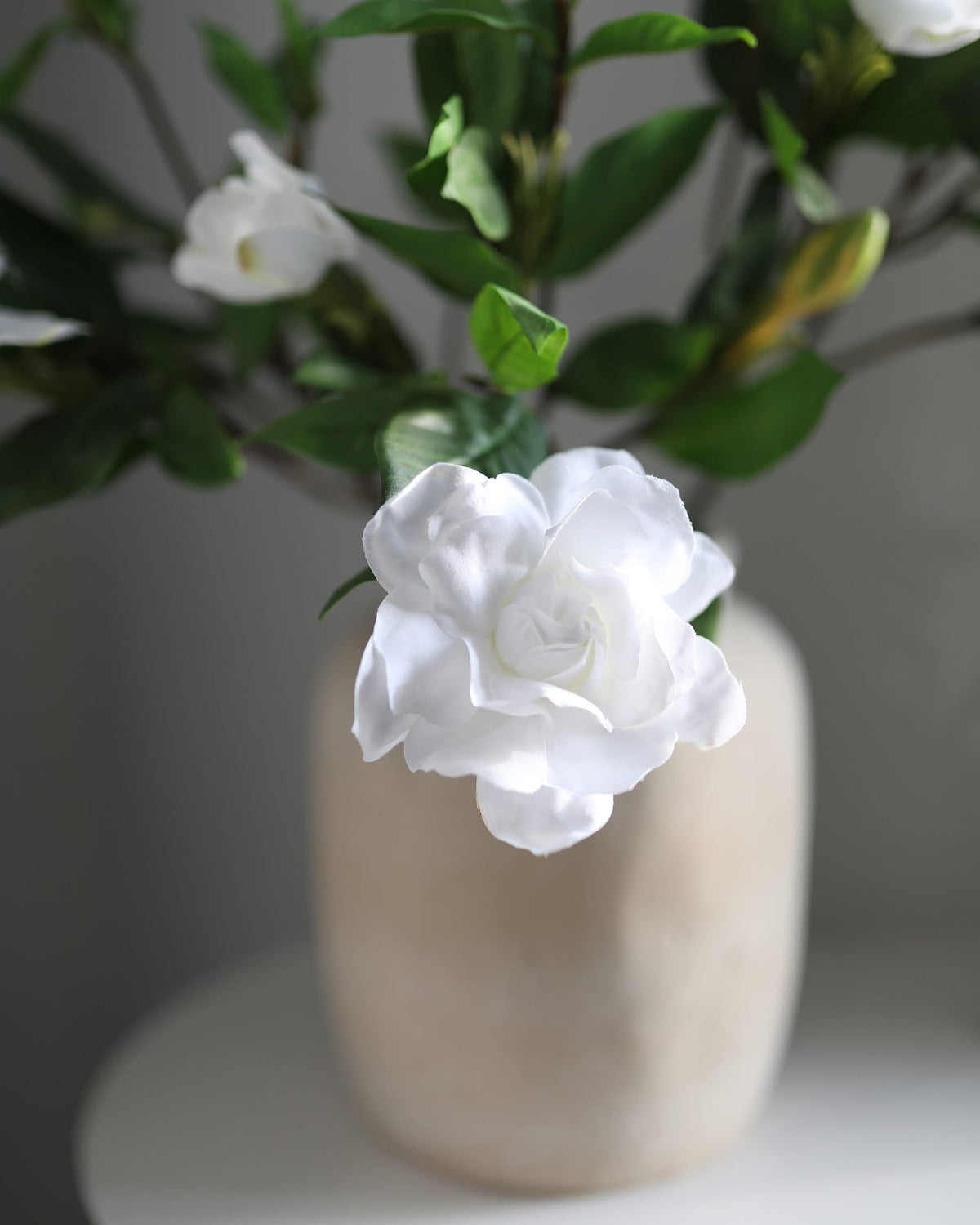 Artificial gardenia in a beige vase against a neutral background