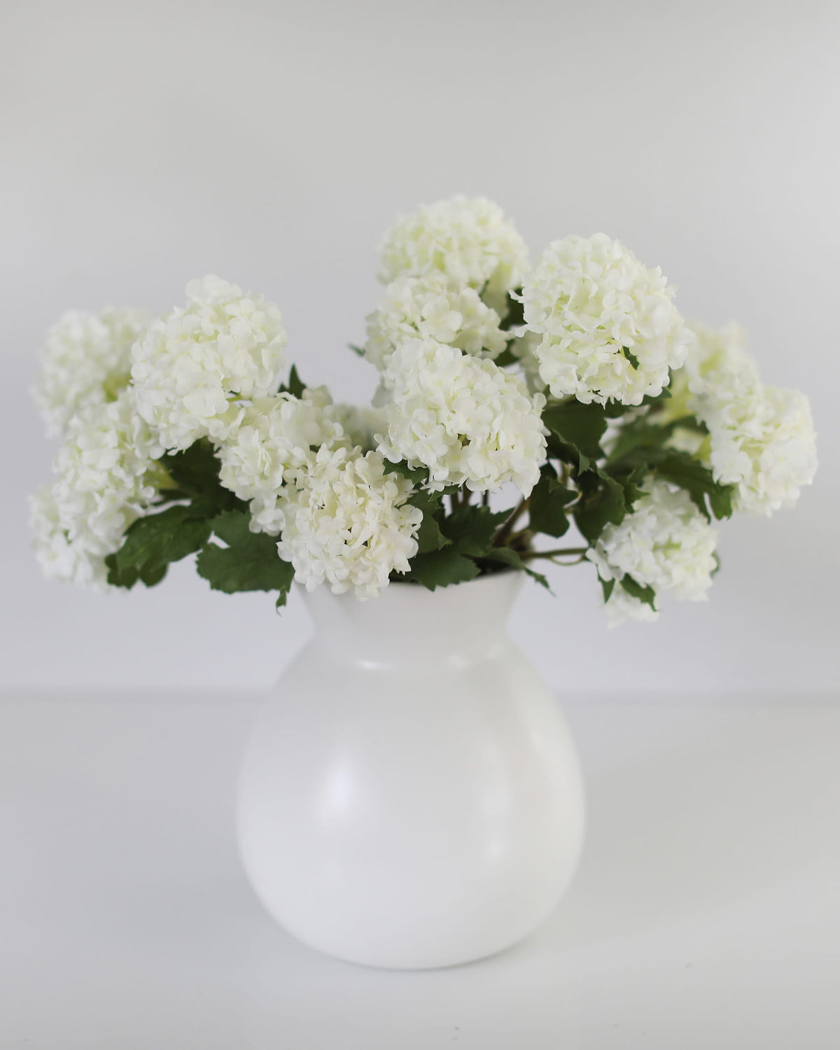 White vase with white artificial snowballs on a light gray background
