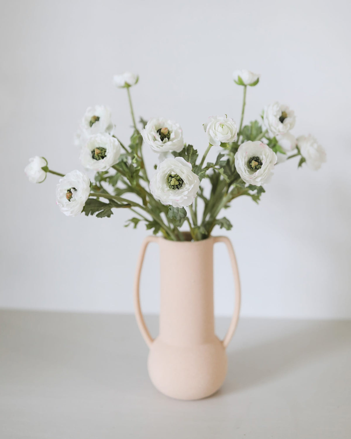 Pink vase with white faux ranunculus on a light background