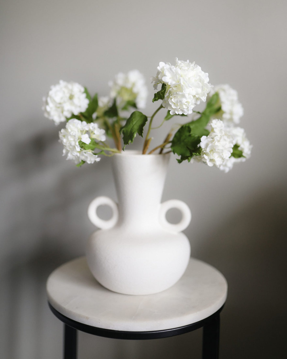 White vase with white artificial snowballs on a marble surface against a gray background