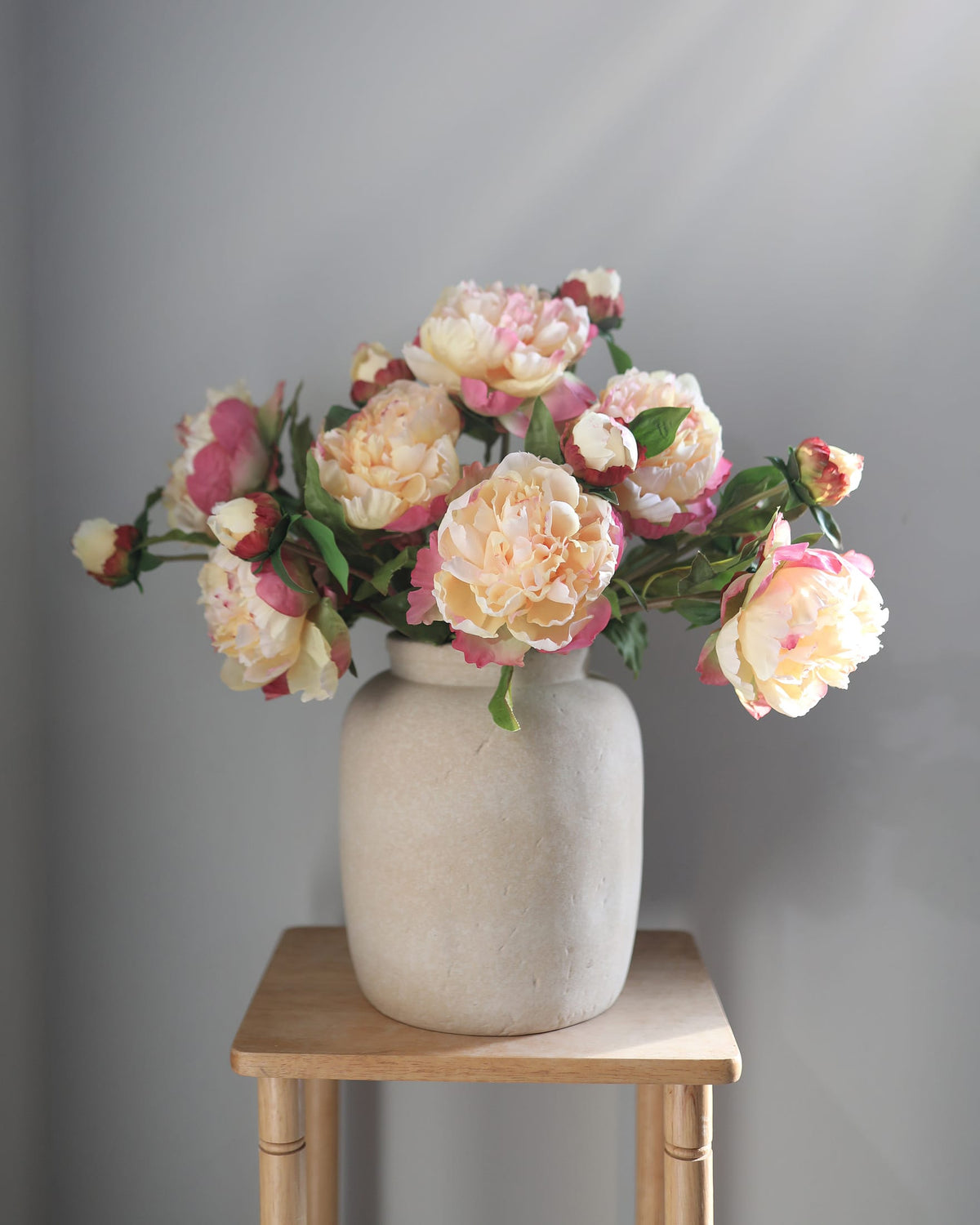 Vase with pink and white flowers on a wooden stool against a gray background
