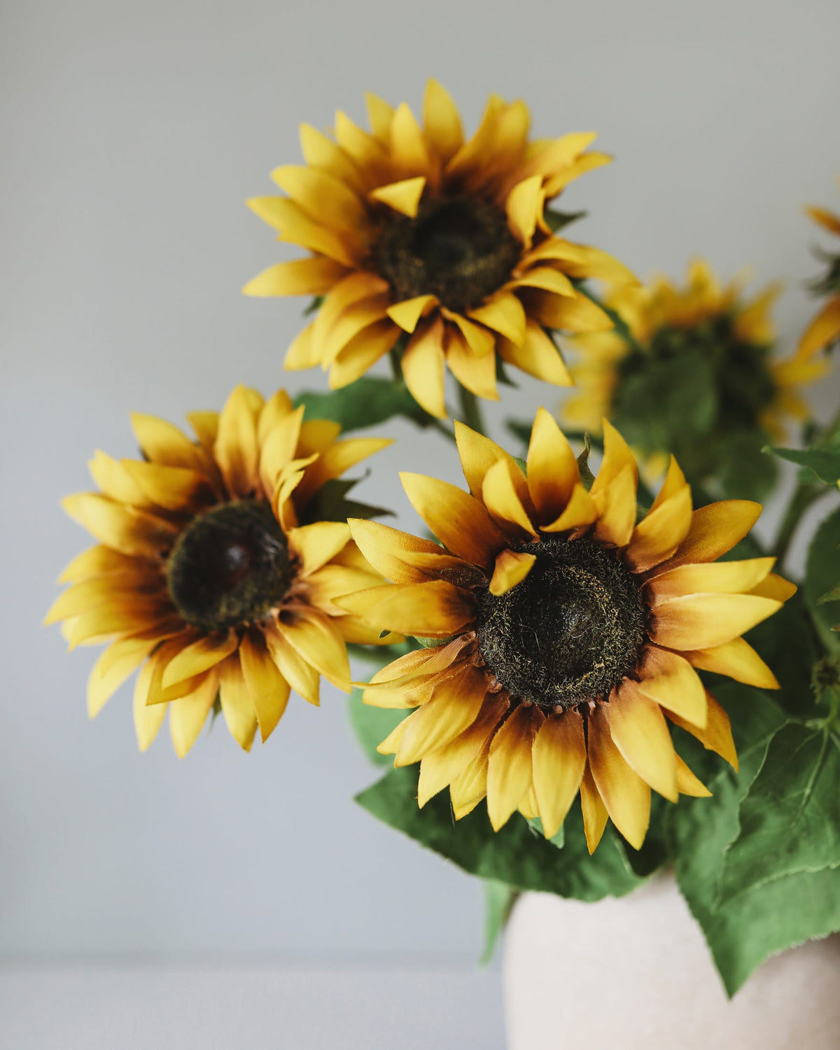 Three faux sunflowers in a vase against a light gray background
